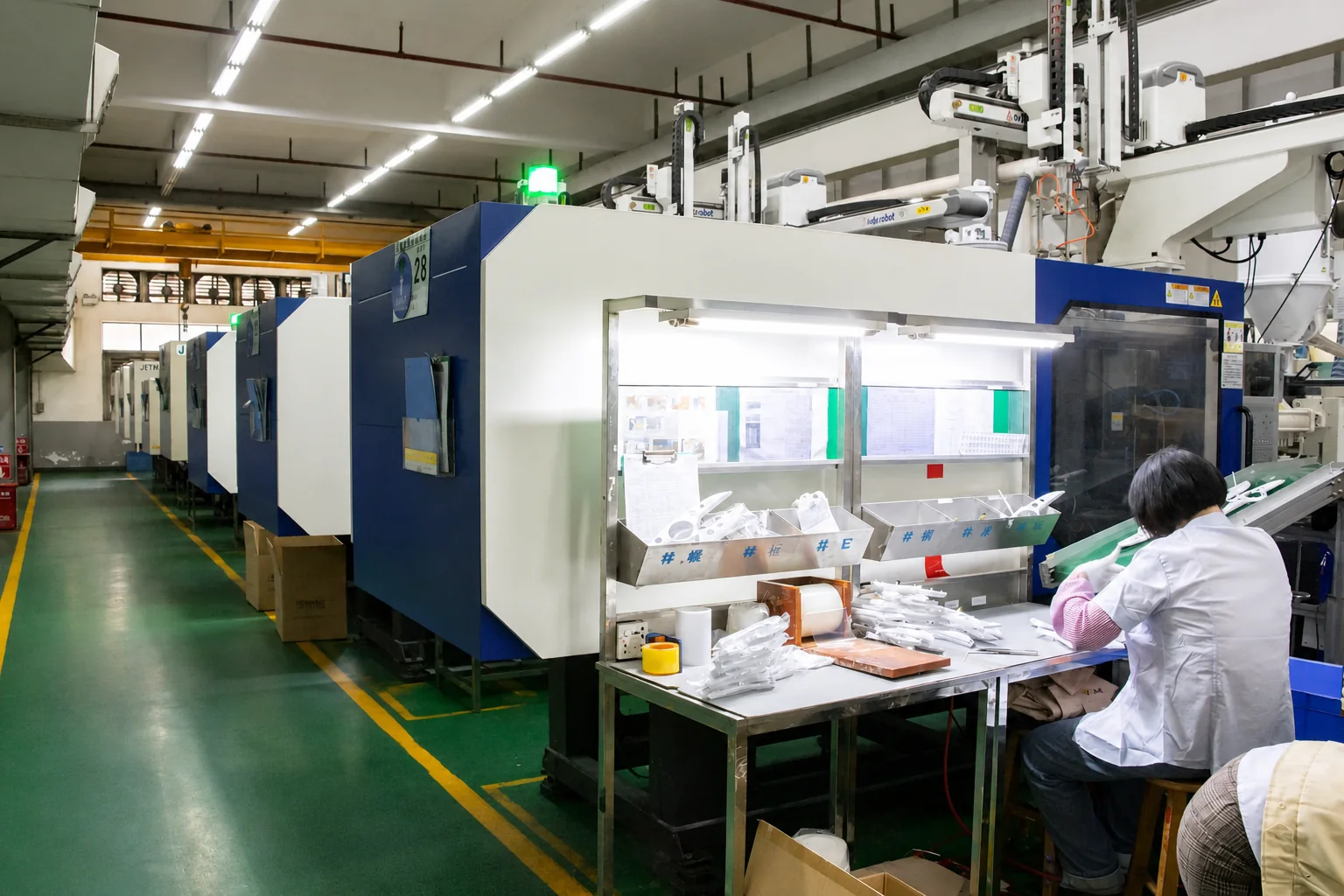 Operator checking molded components at an illuminated workbench beside the molding line