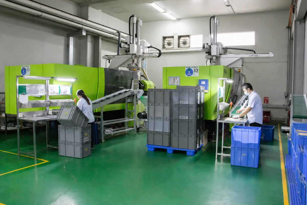 Operators inspecting molded bins at controlled workstations beside the press