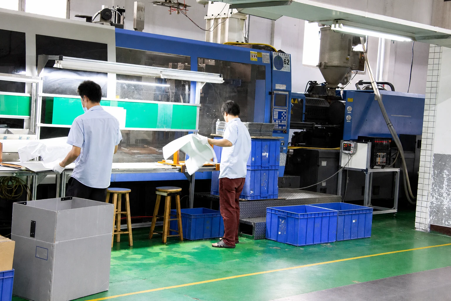 Operators reviewing large molded components beside an active molding cell